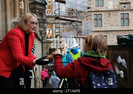 12. Oktober 2023, Niedersachsen, Osnabrück: Bürgermeisterin Katharina Pötter (CDU) präsentiert Schülerinnen und Schülern Brezeln auf den Stufen des Rathauses. Grundschulkinder hatten zuvor ihre Hobbypferde durch die Altstadt von Osnabrück geritten. Der Hobbyritt findet seit 1953 statt. Der Brauch findet jedes Jahr zum Gedenken an den Westfälischen Frieden 1648 statt. Foto: Friso Gentsch/dpa Stockfoto