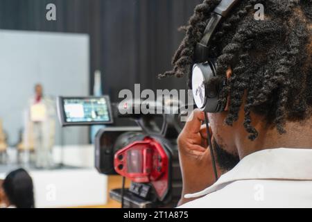 afrikanischer Kameramann mit Dreadlocks und Kamera, die ein Ereignis in Innenräumen filmt Stockfoto