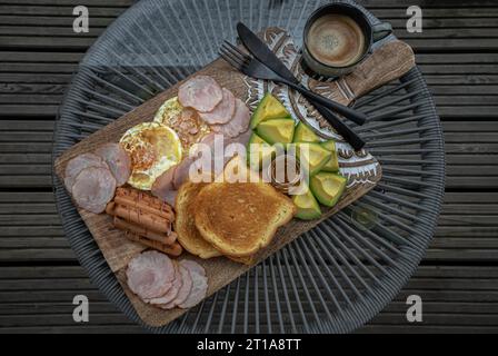 Das Frühstück umfasst gebratene Würstchen, gebratene Eier, Toastbrot und geschnittene Avocados, serviert mit Honig und einer Tasse Kaffee. Draufsicht, Abstand für Text, Auswählen Stockfoto