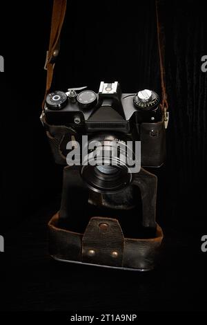 Eine alte Film-SLR-Kamera in einem abgenutzten Lederetui auf dunklem Hintergrund Stockfoto