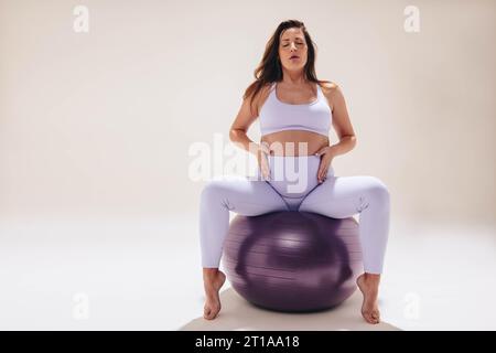 Werdende Mutter übt pränatalen Yoga mit einem Stabilitätsball für Bewegung und Flexibilität. Mit achtsamem Atmen und Fitnesskleidung setzt sie Prioritäten Stockfoto