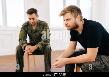 Porträt eines jungen bärtigen Veteranen in Tarnuniform mit Behinderung, der PTBS-Unterstützungsgruppe besucht und über seine Erfahrungen spricht. Stockfoto