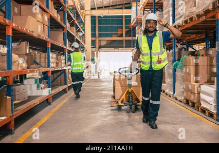 Lagermitarbeiter, die mit einem Handhubwagen oder einer Paketzustellung mit Handhubwagen vom Warenregallagerbereich aus versandt werden. Stockfoto