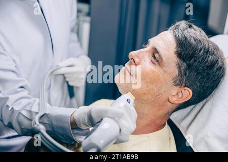Hautarzt mit Laser-Resurfacing Gesichtshaut-Behandlungstechnologie mit erwachsenen Männern, um Falten und Narben in der Anti-Aging-Klinik zu reduzieren Stockfoto