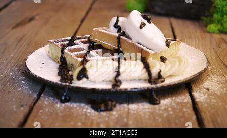 Weiche belgische Waffeln mit Schokoladenbelag beträufeln, während Dessert zubereitet wird. Machen Sie Süßigkeiten aus weichen Waffeln und süßem Eis Stockfoto