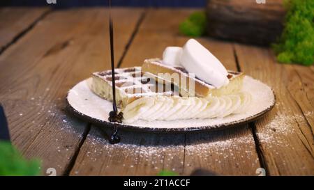 Weiche belgische Waffeln mit Schokoladenbelag beträufeln, während Dessert zubereitet wird. Machen Sie Süßigkeiten aus weichen Waffeln und süßem Eis Stockfoto