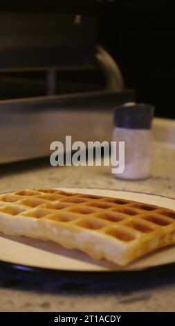 Weiche belgische Waffeln mit Schokoladenbelag beträufeln, während Dessert zubereitet wird. Machen Sie Süßigkeiten aus weichen Waffeln und süßem Eis Stockfoto
