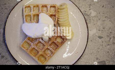 Weiche belgische Waffeln mit Schokoladenbelag beträufeln, während Dessert zubereitet wird. Machen Sie Süßigkeiten aus weichen Waffeln und süßem Eis Stockfoto