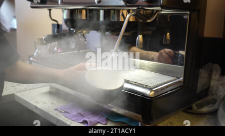 Blasen des Dampfrohrs der Kaffeemaschine. Desinfektion von Geschirr mit Dampf aus einer Kaffeemaschine. Pflege der Sauberkeit und Hygiene in der Bar Stockfoto