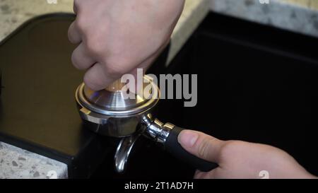 Zubereitung von gemahlenem Kaffee mit Tamping von frischem Kaffee. Manipulation von frisch gemahlenem Kaffee. Die Hand eines Baristas hält und drückt das gemahlene Kaffeepulver Stockfoto