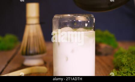 Der Barista gießt Matcha-Grüntee mit Milch und Eis in ein Glas. Cafe Kellnerin serviert kalten Matcha-grünen Tee an einem Gast am Café-Theke. Die Co Stockfoto