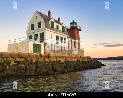 Sonnenuntergang im Herbst am Rockland Breakwater Lighthouse in Maine vom Wasser aus gesehen. Historisches Gebäude mit Holz-, Stein- und Backsteinarchitektur. Stockfoto