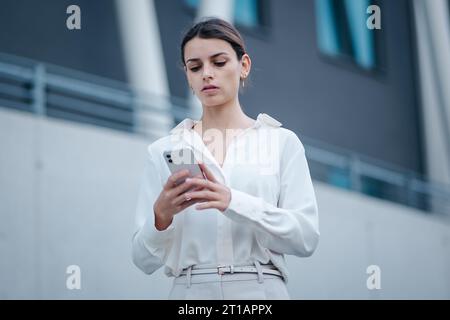 Eine junge Frau, die auf ihrem Handy tippt, steht mitten in einer Stadtstraße Stockfoto