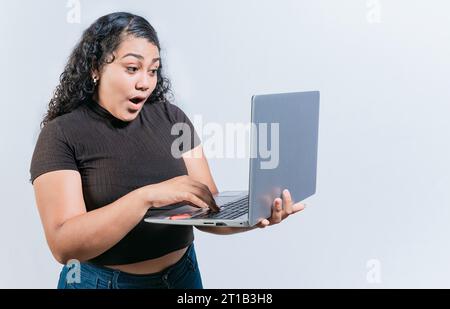 Verblüffte lateinfrau, die einen Laptop isoliert benutzte. Überraschtes Mädchen, das auf einem Laptop-Bildschirm eine Promotion ansieht Stockfoto
