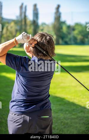 Rückansicht einer Golferin, die an einem sonnigen Tag in der Schweiz einen Golfschaukel macht Stockfoto