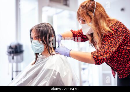 Friseur mit Maske und Handschuhen schneidet dem Kunden die Enden mit einer Schere ab. Wiederaufnahme mit Sicherheitsmaßnahmen für Friseure im COVID-19 Stockfoto