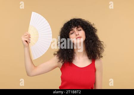 Frau mit Handventilator, die unter Hitze auf beigem Hintergrund leidet Stockfoto