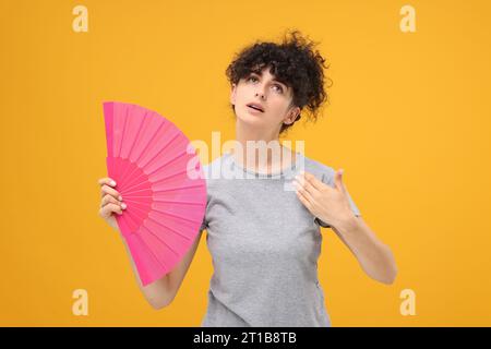 Frau mit Handventilator, die an Hitze auf orangem Hintergrund leidet Stockfoto