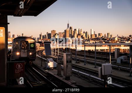 Golden-Hour-Blick auf die Skyline von New York City und einen sich nähernden G-Zug bei Sunrise auf dem erhöhten Eisenbahnabschnitt der G-Linie an der Smith Street. Stockfoto
