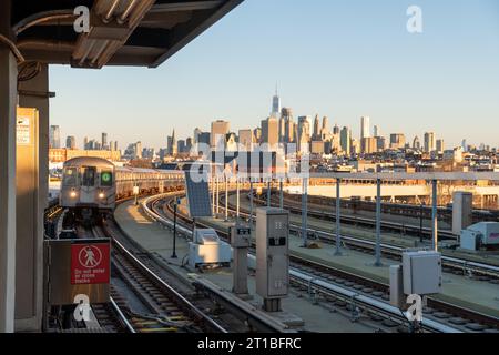 Golden-Hour-Blick auf die Skyline von New York City und einen sich nähernden G-Zug bei Sunrise auf dem erhöhten Eisenbahnabschnitt der G-Linie an der Smith Street. Stockfoto
