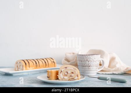 Stücke süßer Schwammkuchen Rolle und Tasse mit Tee auf Tisch vor weißem Hintergrund Stockfoto