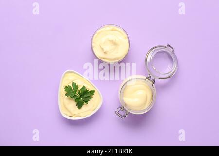 Schüsseln und ein Glas frischer Mayonnaise auf Fliederhintergrund Stockfoto