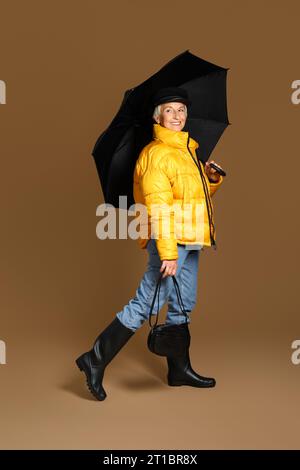 Schöne reife Frau mit Regenschirm auf braunem Hintergrund Stockfoto