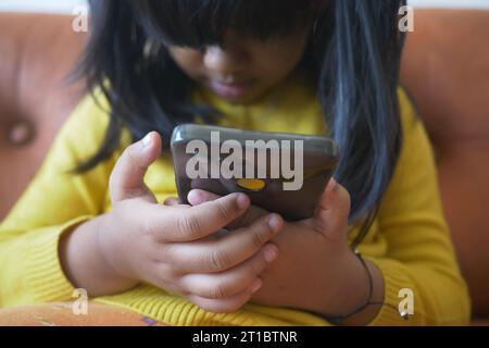 Kind Mädchen in gelbem Kleid, das Cartoon auf dem Smartphone ansieht Stockfoto