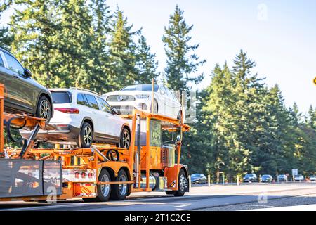 Orangefarbener Industrietransportwagen, großer Lkw mit verlängerter Fahrerkabine für Lkw-Fahrer, der Autos auf hydraulischem Auflieger transportiert, läuft Stockfoto