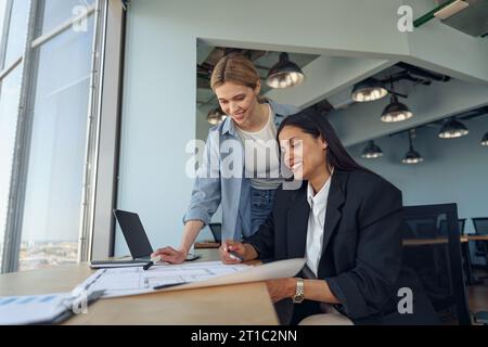 Zwei weibliche Kollegen diskutieren das Projekt, bevor sie der Teamleiterin im Büro eine Präsentation zeigen Stockfoto