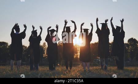 College-Absolventen in Gewändern, die bei Sonnenuntergang winken. Stockfoto