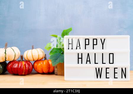 Leuchtkasten mit Nachricht HAPPY HALLOWEEN gerahmt und Kürbisse mit grünen Blättern auf blauem Hintergrund Stockfoto