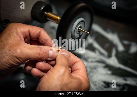 Ein Goldschmied poliert in seiner Schmuckwerkstatt einen Goldring. Juwelierhände arbeiten in seinem Kunsthandwerksstudio. Stockfoto