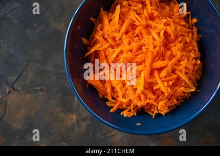 Geriebene Karotten in einem blauen Teller auf dunklem Hintergrund. Stockfoto