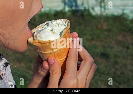 Kind beißt in der Natur eine Waffeltasse mit Pistazieneis Stockfoto