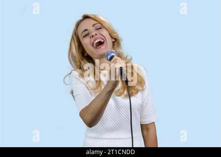 Porträt einer glücklichen reiferen blonden Frau, die im Mikrofon singt. Isoliert auf blassblau. Stockfoto