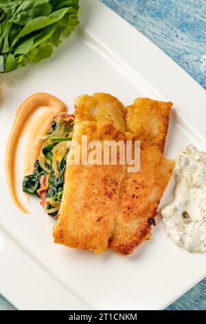 Gebratenes Panga-Filet mit Gemüse und Zwiebeln an der Seite und Spinat darunter Stockfoto