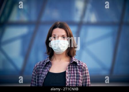 Frau in Maske auf der Straße wegen Coronavirus-Epidemie in der Stadt. Modernes Gebäude im Hintergrund. Schutz vor Viren und Infektionen. Stockfoto