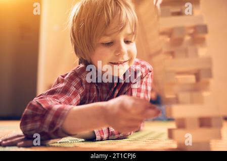 Kindergartenjunge, der zu Hause mit Holzblöcken spielt. Die Spieler müssen abwechselnd einen Block nach dem anderen aus einem Turm entfernen. Jeder Block wird entfernt Stockfoto