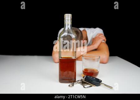 Autoschlüssel und Alkohol auf dem Tisch. Betrunkener Mann, der auf dem Tisch mit einer Flasche Whiskey und Drink schläft. Alkoholismus. Fahren Sie nicht, wenn Sie betrunken sind. Stockfoto