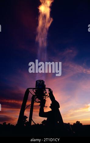 Heißluftballonfahrten. Nahaufnahme der Silhouette eines Mannes in der Nacht mit einem Brenner, der einen Ballon aufbläst. Stockfoto