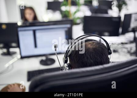 Rückansicht eines jungen Geschäftsmannes mit Kopfhörern am Computertisch im modernen Büro Stockfoto