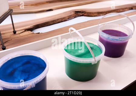 Prozessfertigung eines Kunstharz- und Holztisches. Flüssiges Epoxid wird in eine Form mit Holzrohlingen gegossen. Nahaufnahme Stockfoto