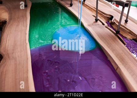 Prozessfertigung eines Kunstharz- und Holztisches. Flüssiges Epoxid wird in eine Form mit Holzrohlingen gegossen. Nahaufnahme Stockfoto