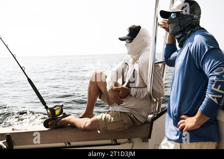 Zwei Fischer blicken auf das Meer, während sie auf einem Fischerboot sitzen. Stockfoto