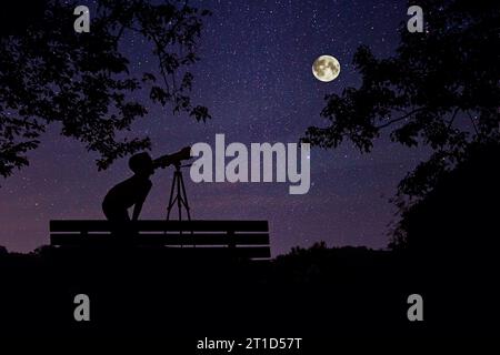 Junge in der Nacht, der Sterne und Vollmond durch ein Teleskop betrachtet. Stockfoto
