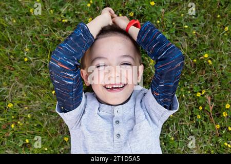 Das Kopfbild eines lachenden Jungen im Gras mit fehlenden Zähnen Stockfoto