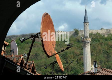 Rostige Satellitenschüsseln auf Dächern in Prizren, Kosovo, mit einem Minarettturm im Hintergrund Stockfoto