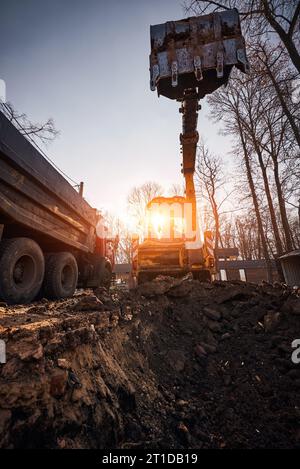 Der Bagger gräbt ein Loch in den Boden, um bei Sonnenuntergang ein Haus zu bauen, keine Leute Stockfoto