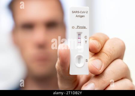 Augsburg, Bayern, Deutschland. Oktober 2023. Der Mann zeigt positiven COVID-19-Coronavirus-Schnelltest. Testkassette mit zwei Linien, Ergebnis-positiv und Variante Pirola-Mutation PHOTOMONTAGE *** Mann zeigt einen positiven COVID-19 Coronavirus Schnelltest. Testkasette mit zwei Strichen, Ergebnis positiv und Variante Pirola Mutation FOTOMONTAGE Credit: Imago/Alamy Live News Stockfoto